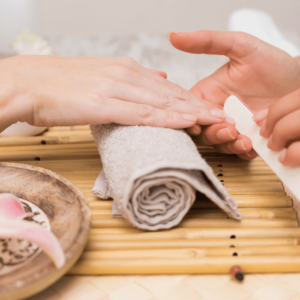 Hands receiving professional nail care treatment on a bamboo mat with a serene spa setting, representing the Nail Technician Diploma course by iStudy.